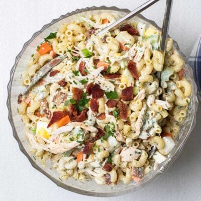 A glass bowl filled with a chicken macaroni salad garnished with crispy bacon and parsley.