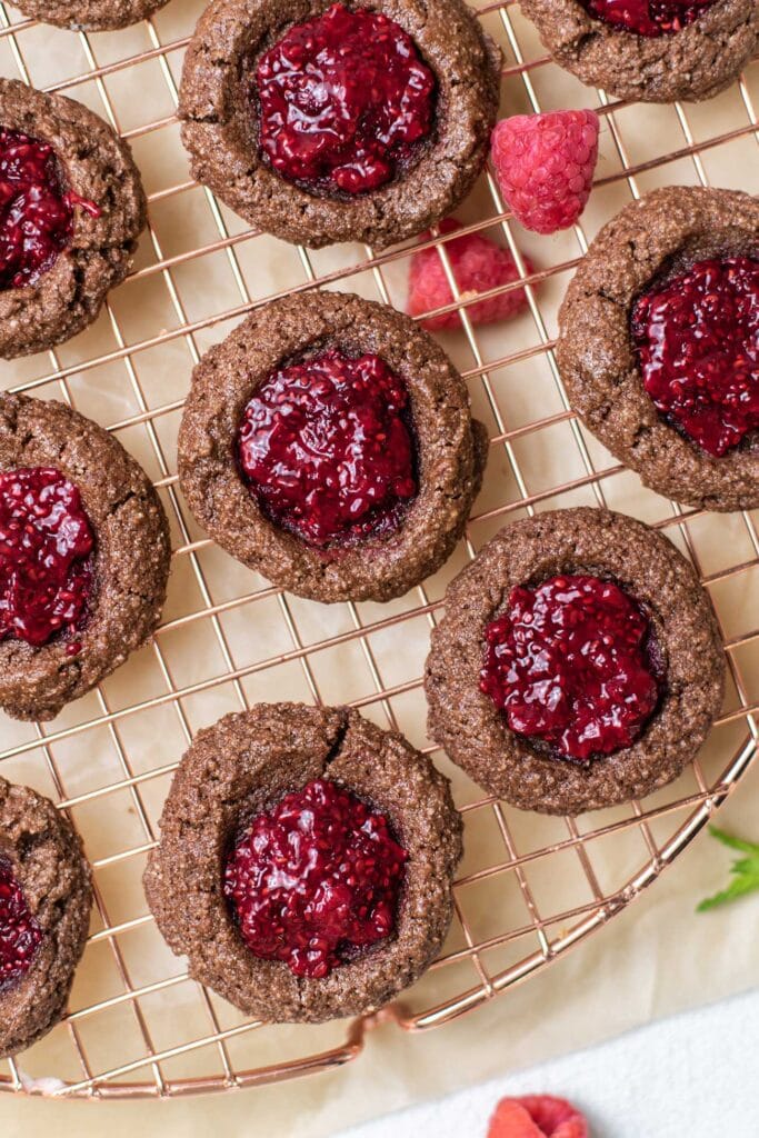 Chocolate thumbprint cookies with raspberry jam shown cooling on a baking rack.