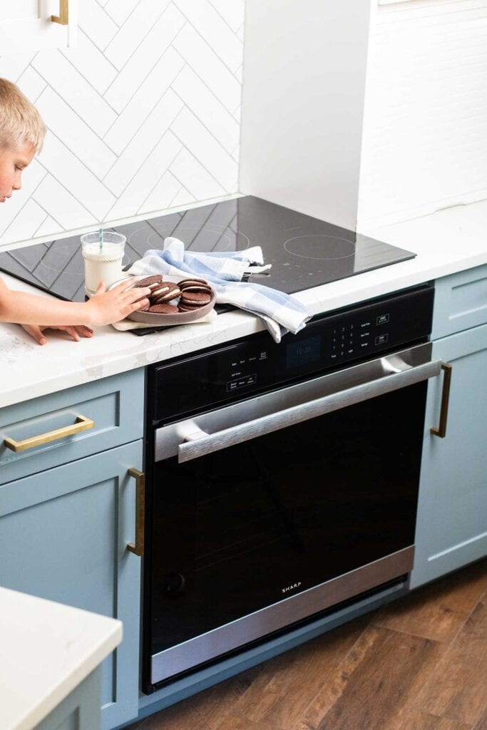 A kid sneaking a cookie off a plate sitting on top of the Sharp European Convection Oven.