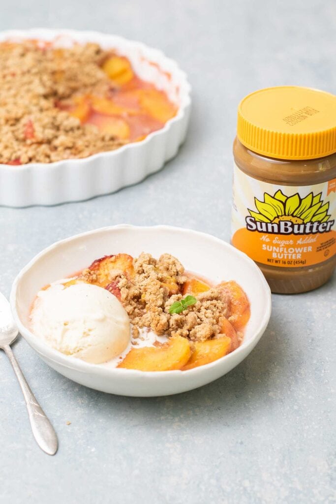 A bowl of peach crumble topped with vanilla ice cream.