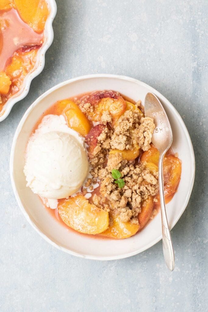 A bowl of peach crumble served with vanilla ice cream.