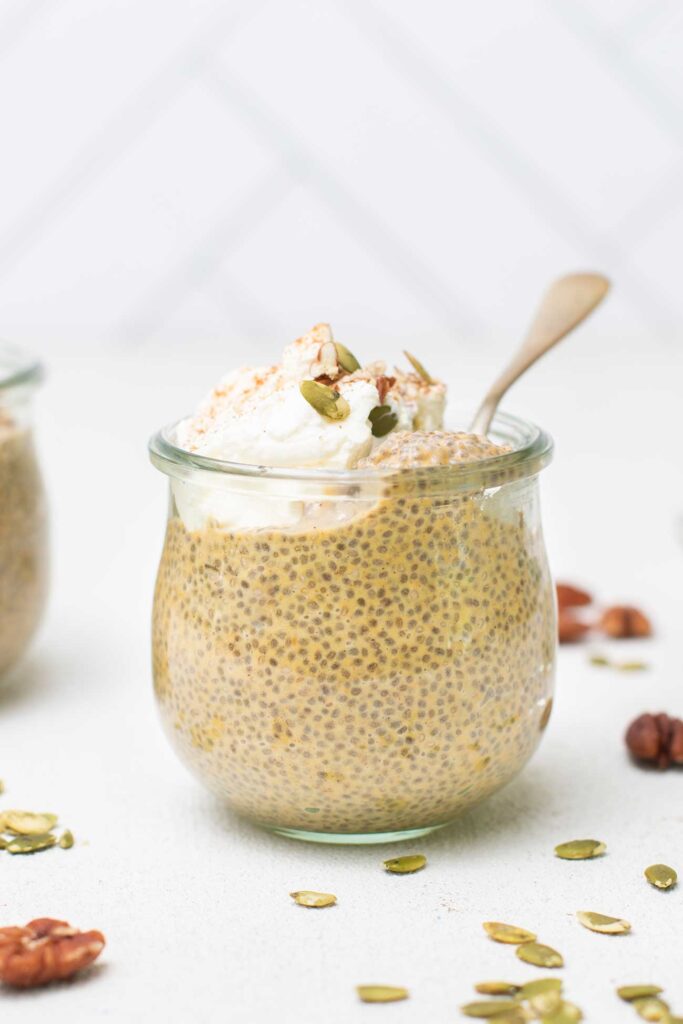 A glass jar of pumpkin chia pudding shown topped with whipped cream and nuts.