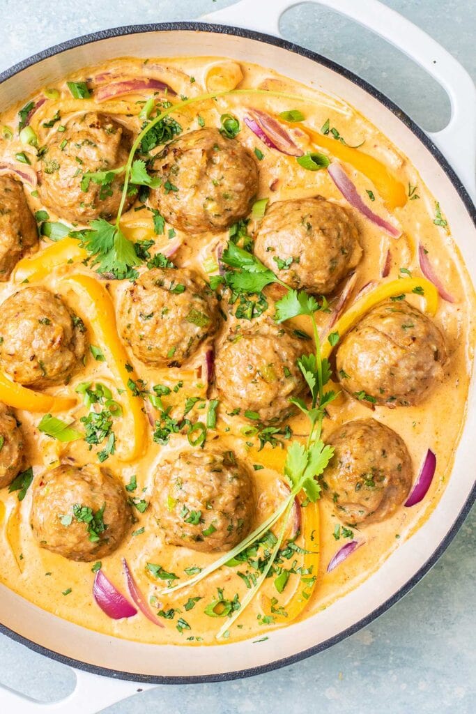 A white cast iron pan filled with a creamy red curry and turkey meatballs.