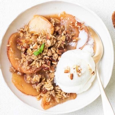 A bowl of gluten free apple crisp topped with vanilla ice cream and pecans.
