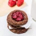 Two gluten free chocolate thumbprint cookies in a stack in front of a glass of almond milk.