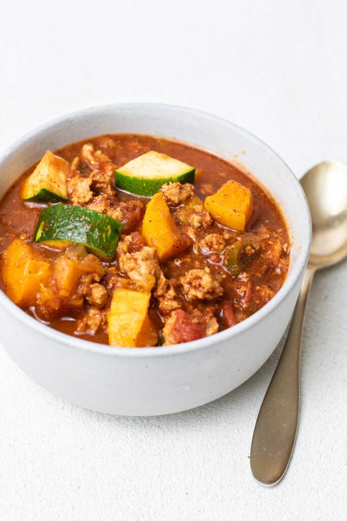 A bowl of butternut and turkey chili shown without garnishes.