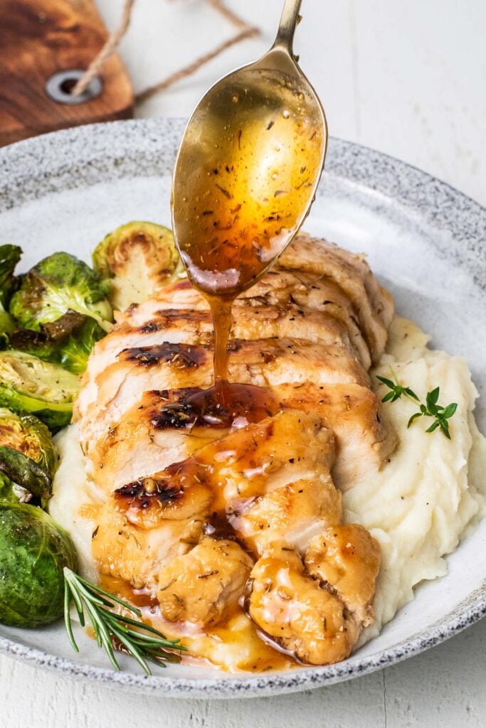 A sliced chicken breast shown being drizzled with a honey balsamic glaze.