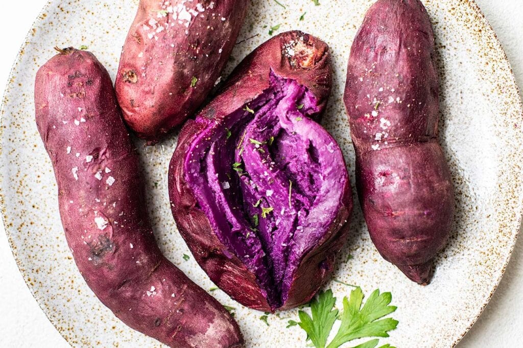 A plate of baked purple sweet potatoes, showing the vibrant purple flesh.