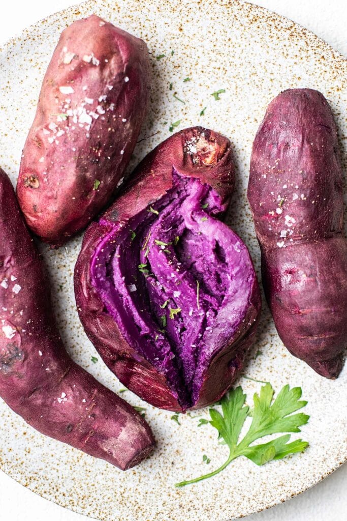 A plate of baked purple sweet potatoes showing the purple hued skins and flesh.