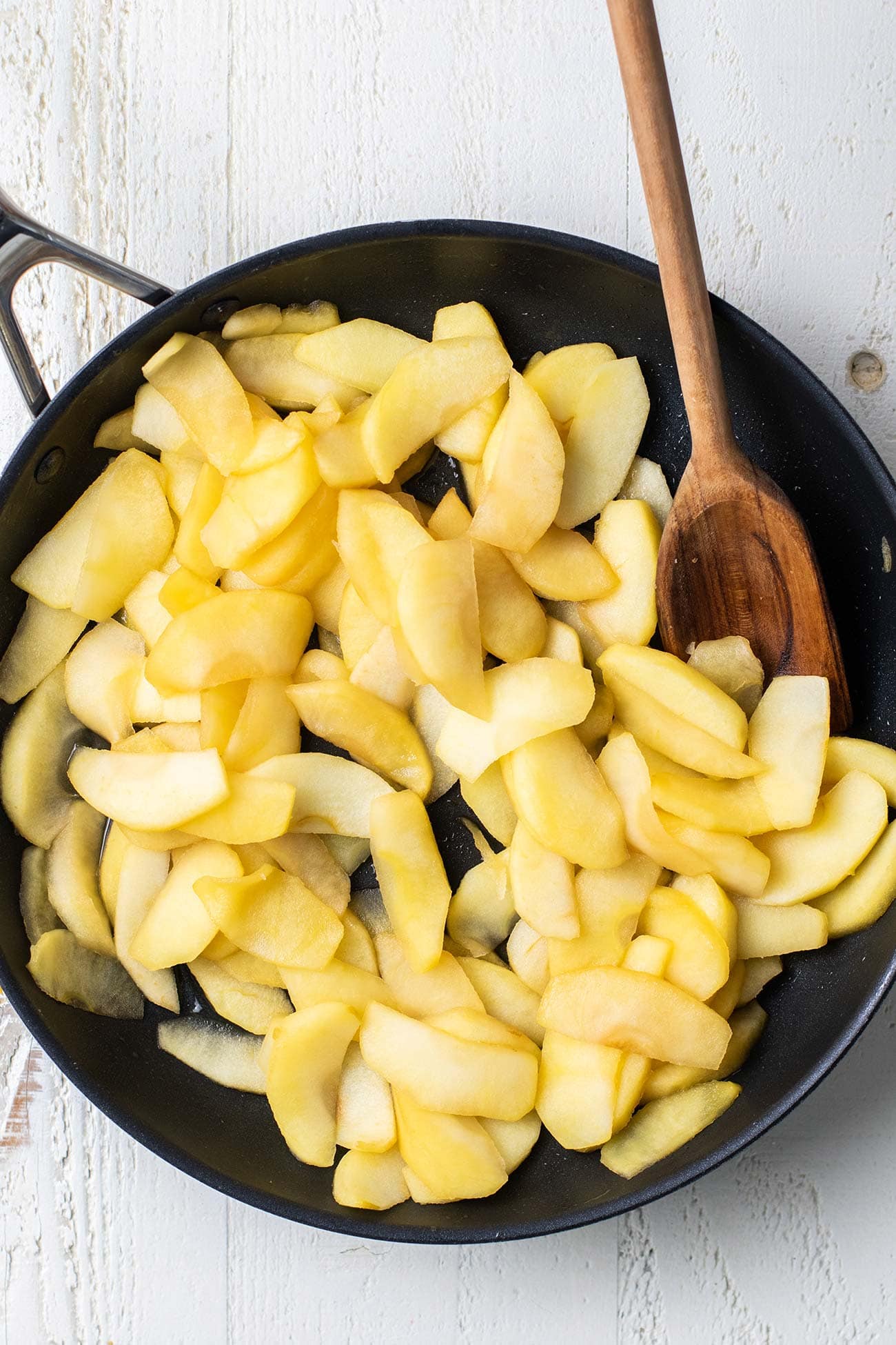Apple slices in a skillet shown being sauteed.