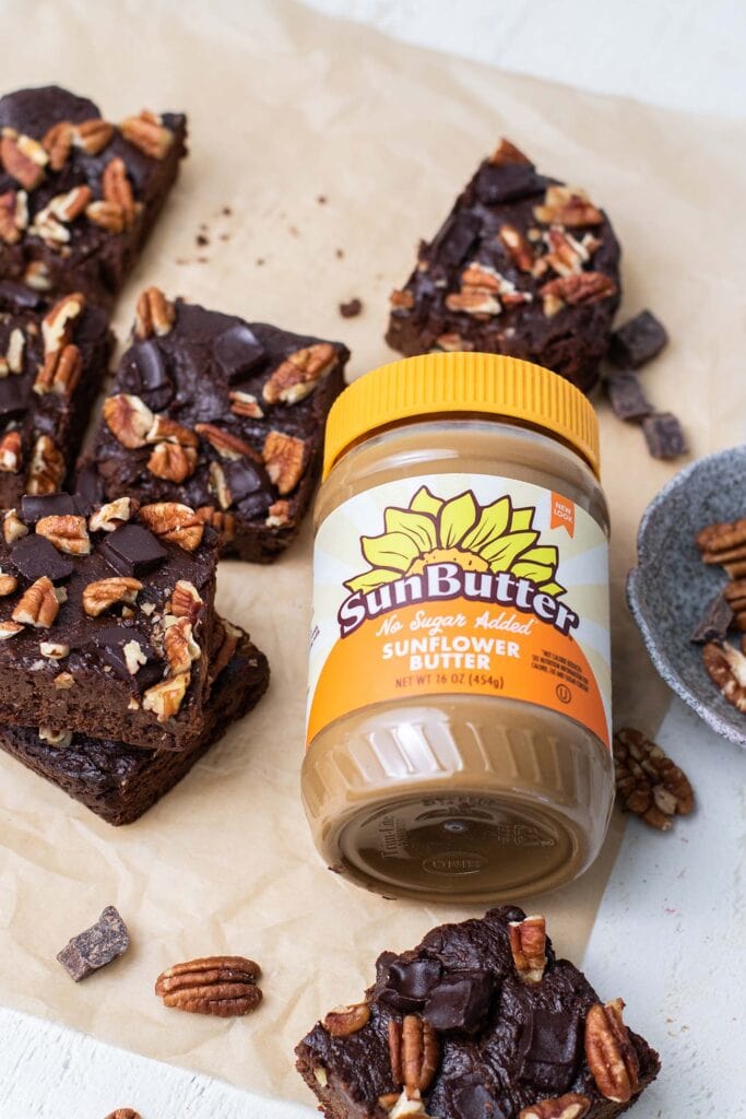 A jar of sunbutter surrounded by fudge brownies cut into squares.