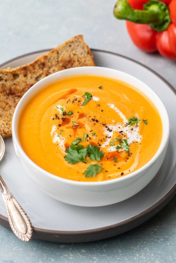 A bowl of vibrant orange sweet potato soup garnished with cilantro and hot sauce.