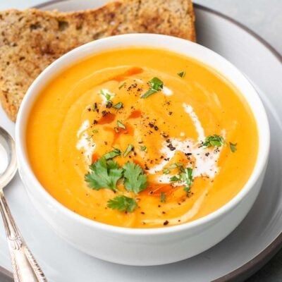 A bowl of sweet potato roasted red pepper soup shown with a slice of buckwheat bread.