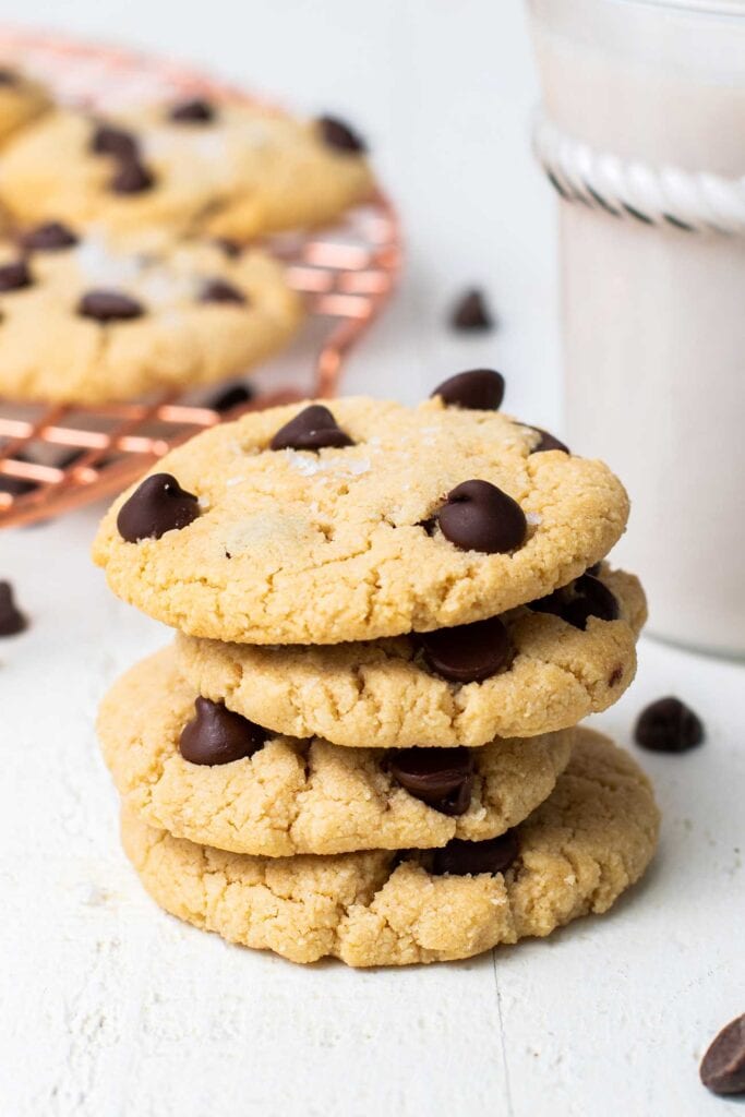A stack of 4 paleo chocolate chip cookies shown sitting in front of a glass of milk.