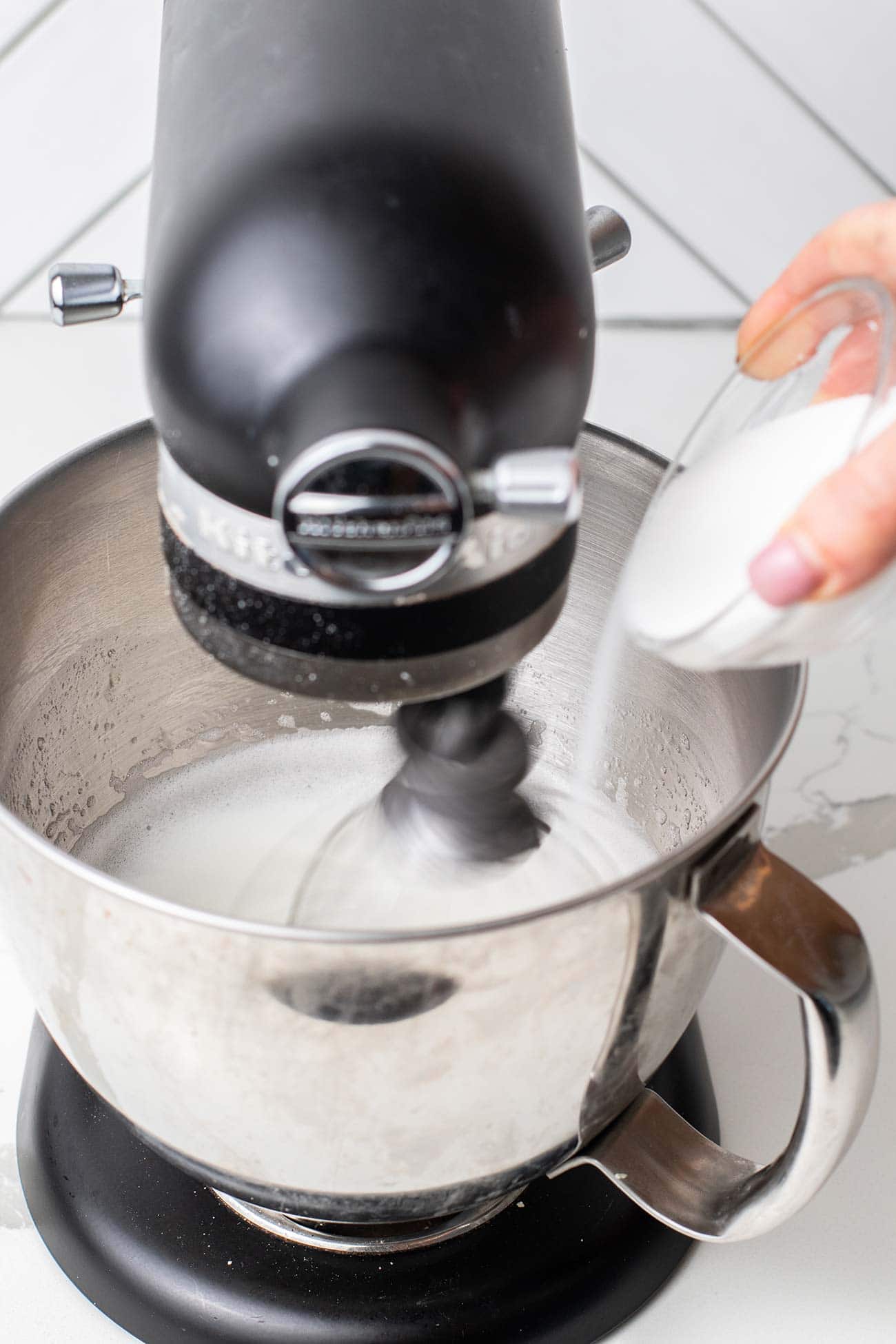 A mixer running with a dish of sugar slowly being poured in.