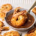 Two baked coconut shrimp sitting in a dish of apricot dipping sauce.