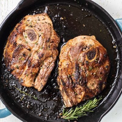 Two lamb shoulder chops shown in a cast iron skillet.