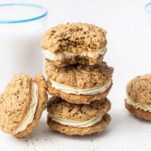 A stack of oatmeal cream pies shown in front of glasses of almond milk.