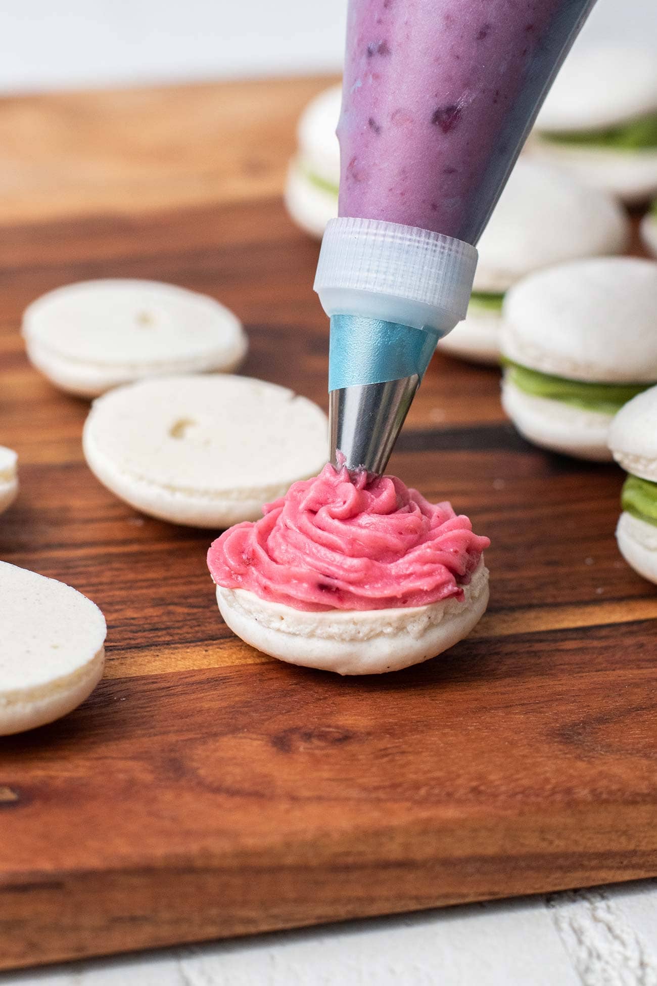 raspberry buttercream being piped onto a macaron shell.
