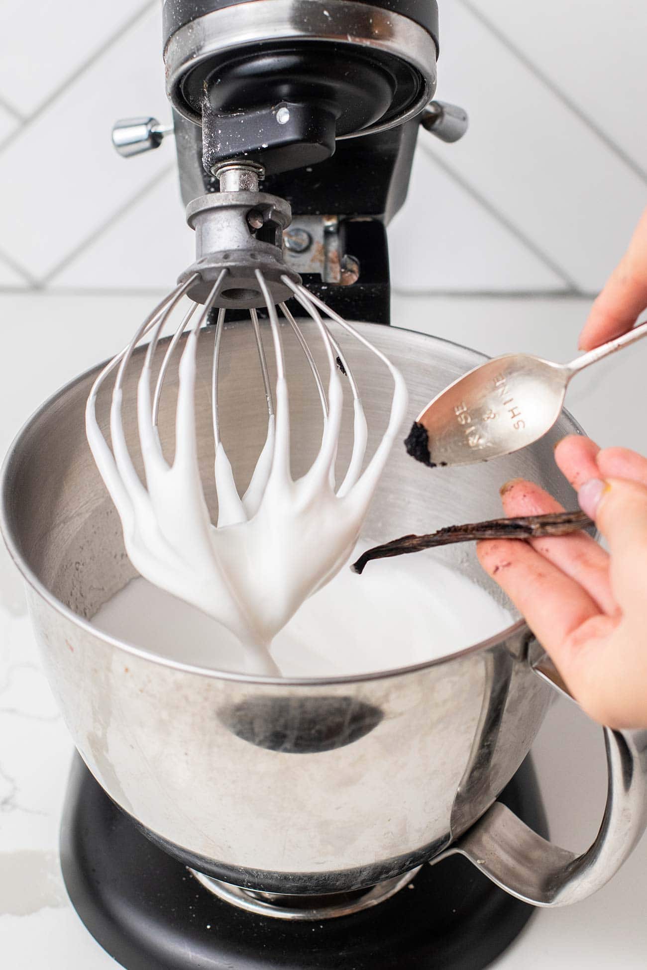 A spoon scraping the vanilla bean into the egg white mixture.