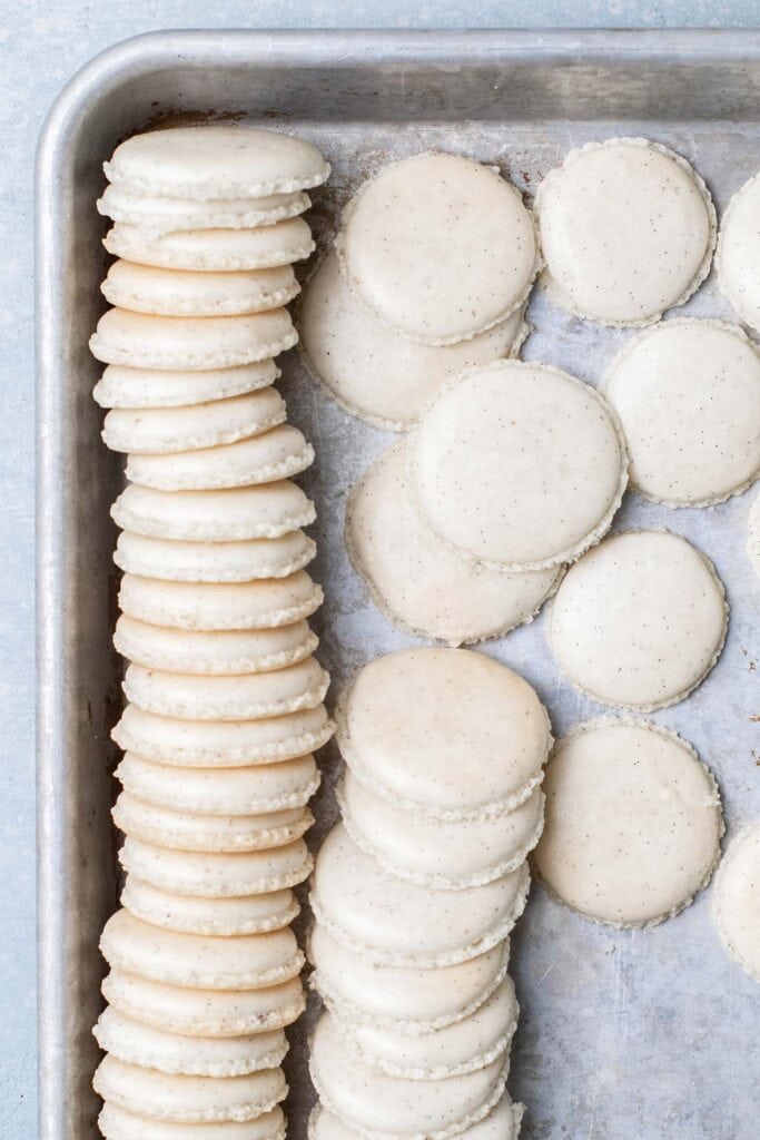 A baking tray with white macarons laid out showing the vanilla bean flecks.