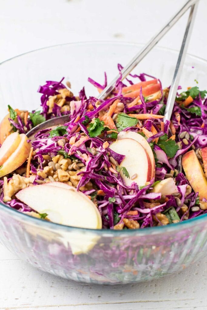 A glass bowl with a purple cabbage salad with apples and walnuts.