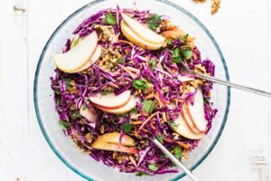 A vibrant red cabbage salad shown garnished with nuts in a class serving bowl.