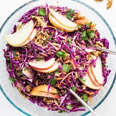 A vibrant red cabbage salad shown garnished with nuts in a class serving bowl.