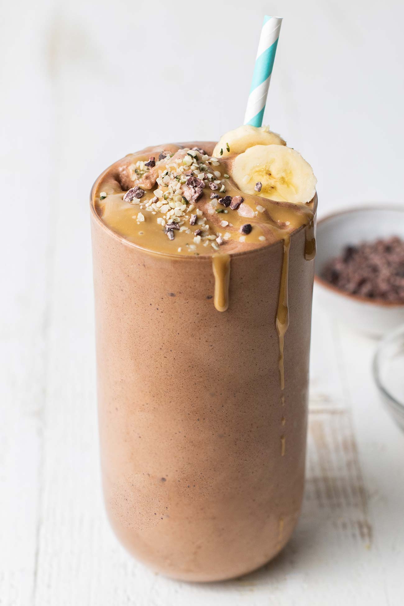 A chocolate banana smoothie shown drizzled with peanut butter and cocoa nibs.