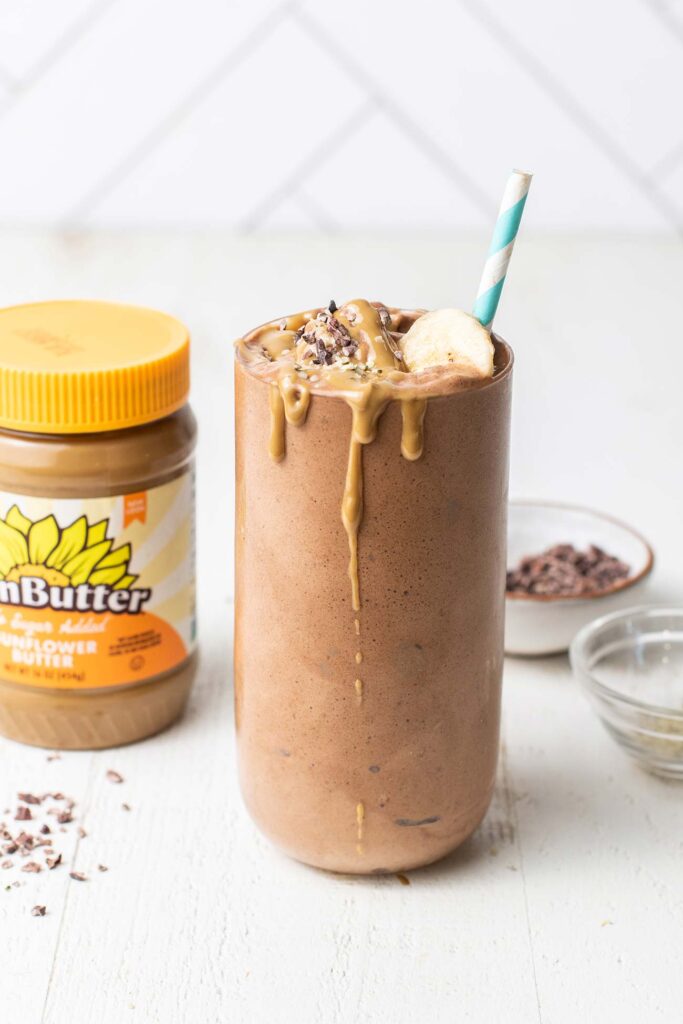 A chocolate smoothie shown sitting next to a jar of nut butter.