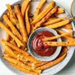 A plate with crisp baked sweet potato fries surrounding a dish of ketchup.