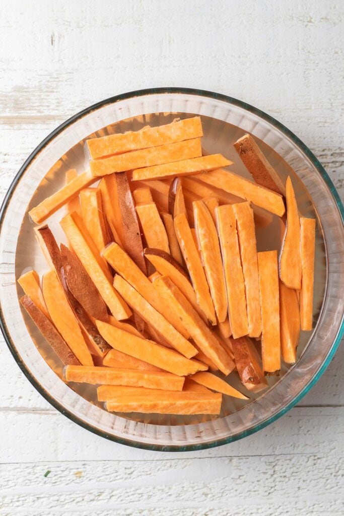 Sweet potato fries shown soaking in a bowl of water.