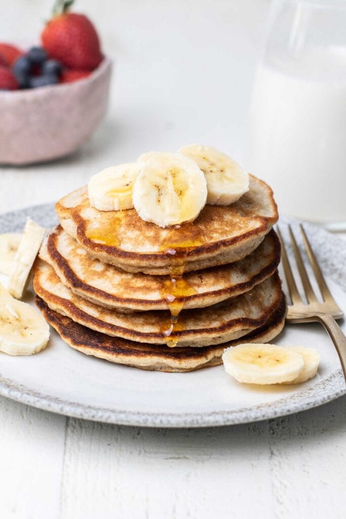 A stack of fluffy buckwheat pancakes shown drizzled with honey and topped with bananas.