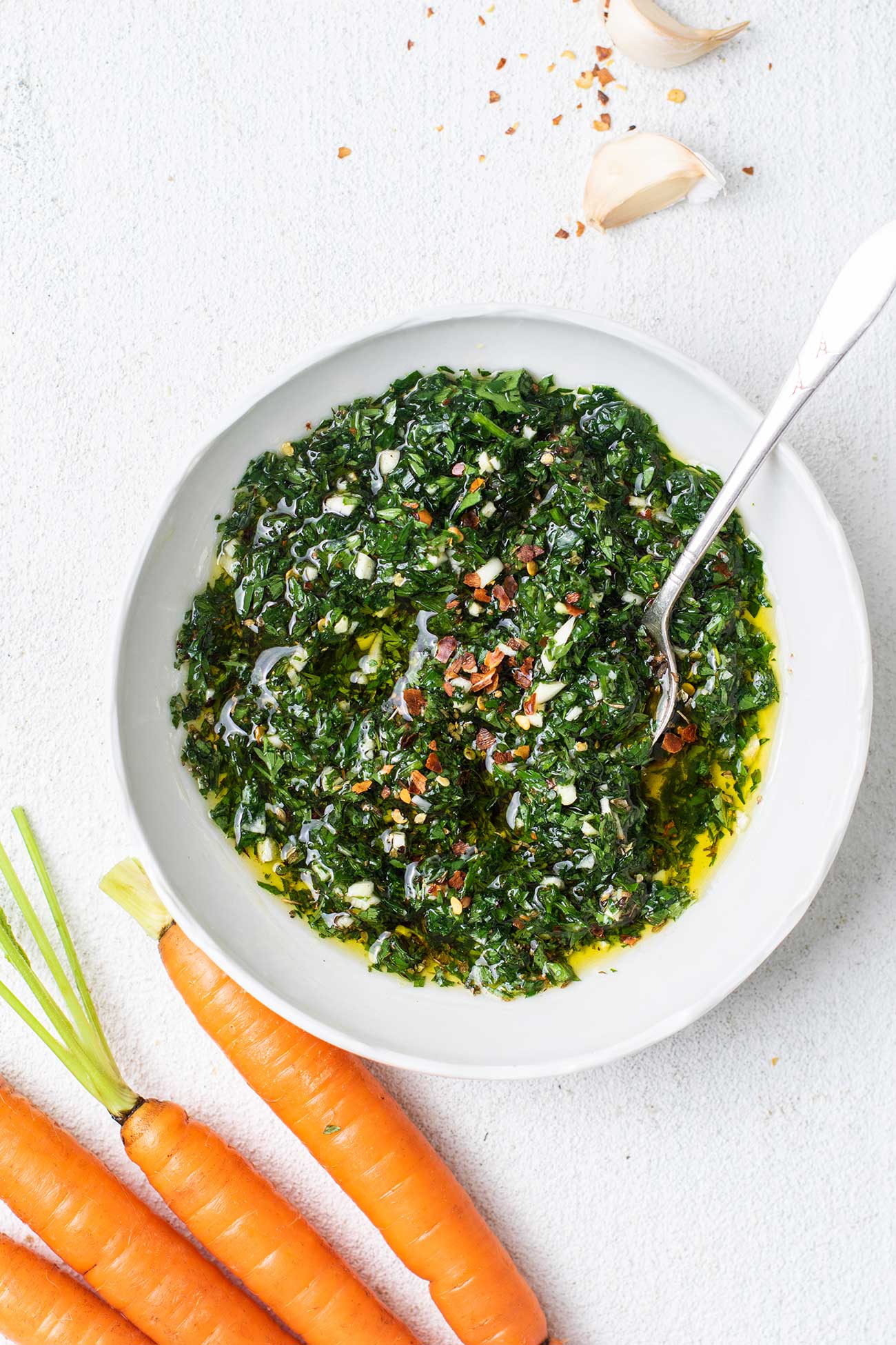A bowl of carrot top chimichurri shown stirred together and garnished with red chili.
