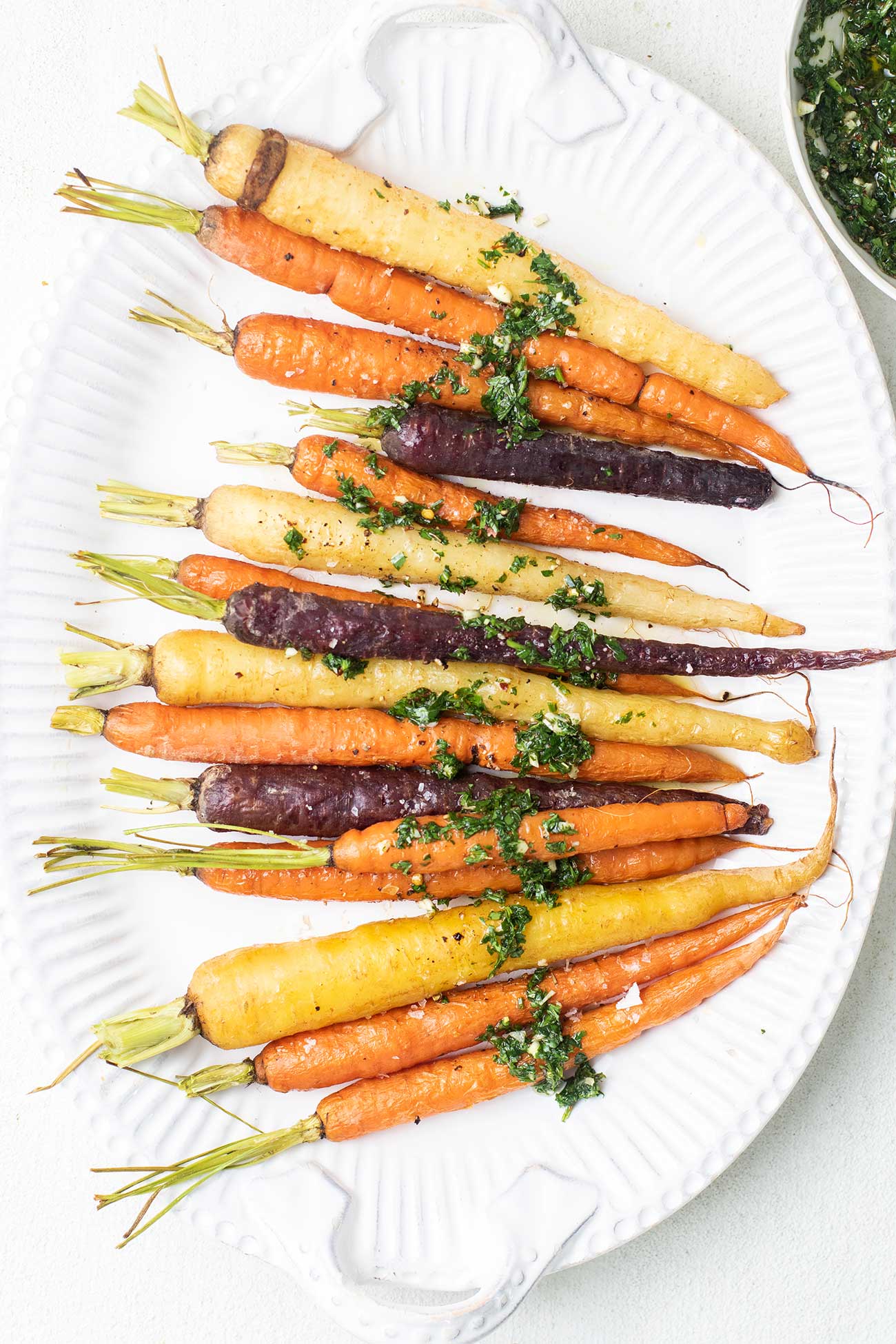 Roasted rainbow carrots shown drizzled with an herby chimichurri.