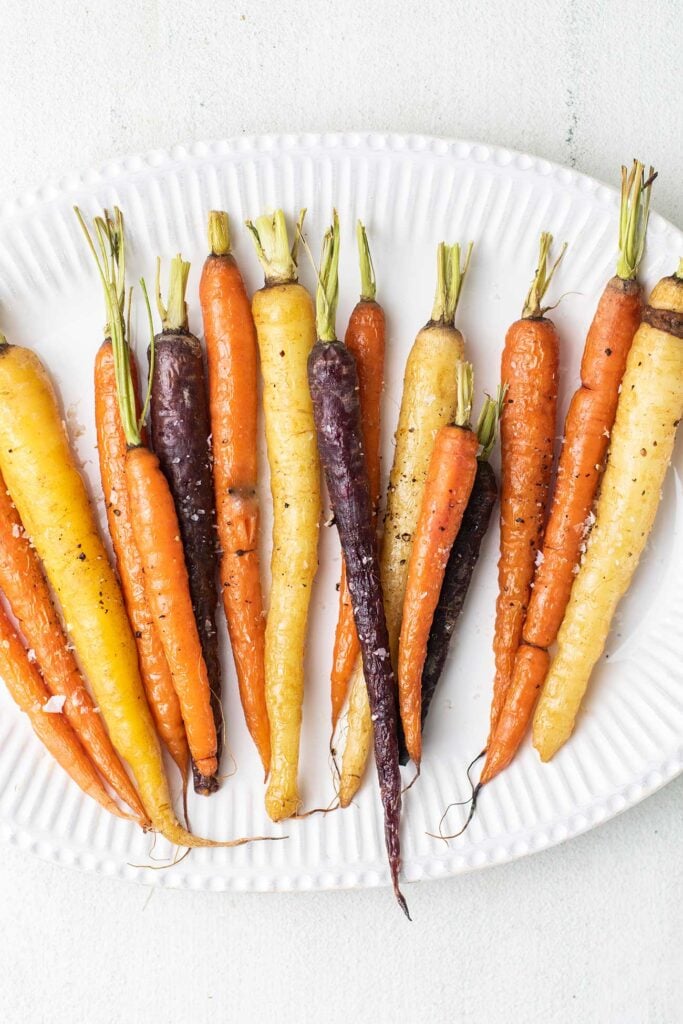 A white platter with roasted rainbow carrots ready to serve.