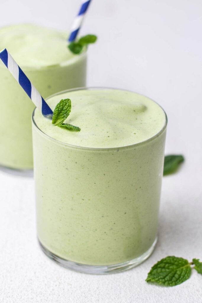 A green mint smoothie shown in a glass garnished with a peppermint leaf.