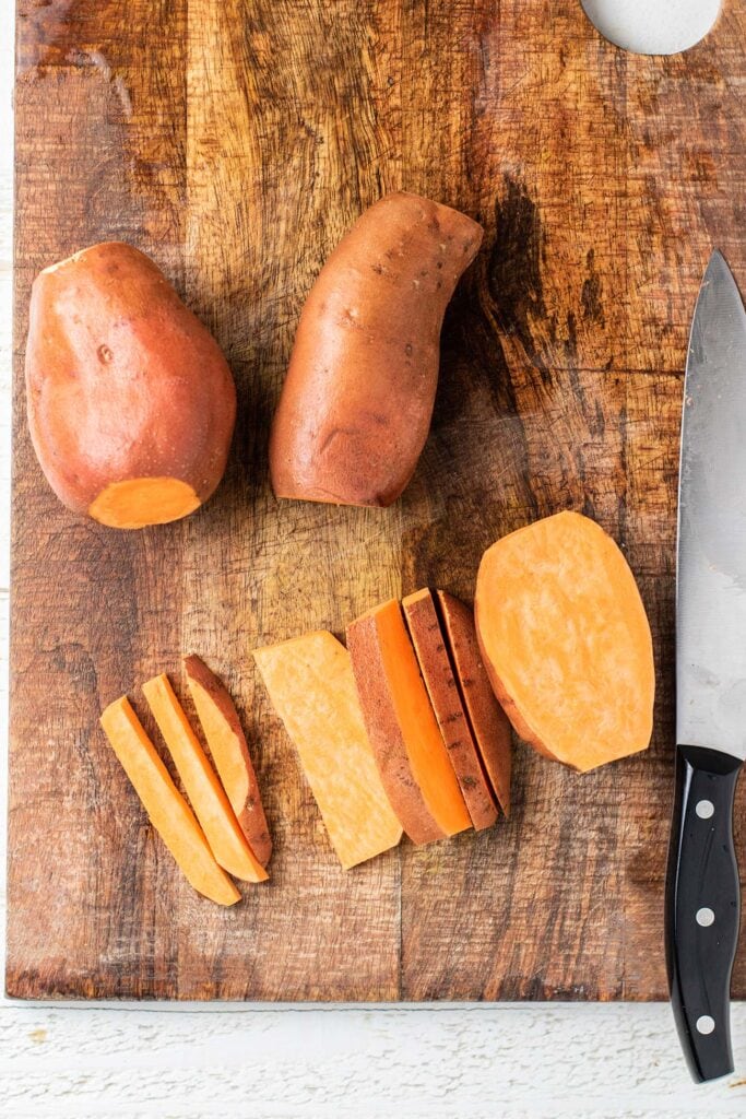 Sweet potatoes on a cutting board showing the process of cutting evenly shaped sweet potato fries.