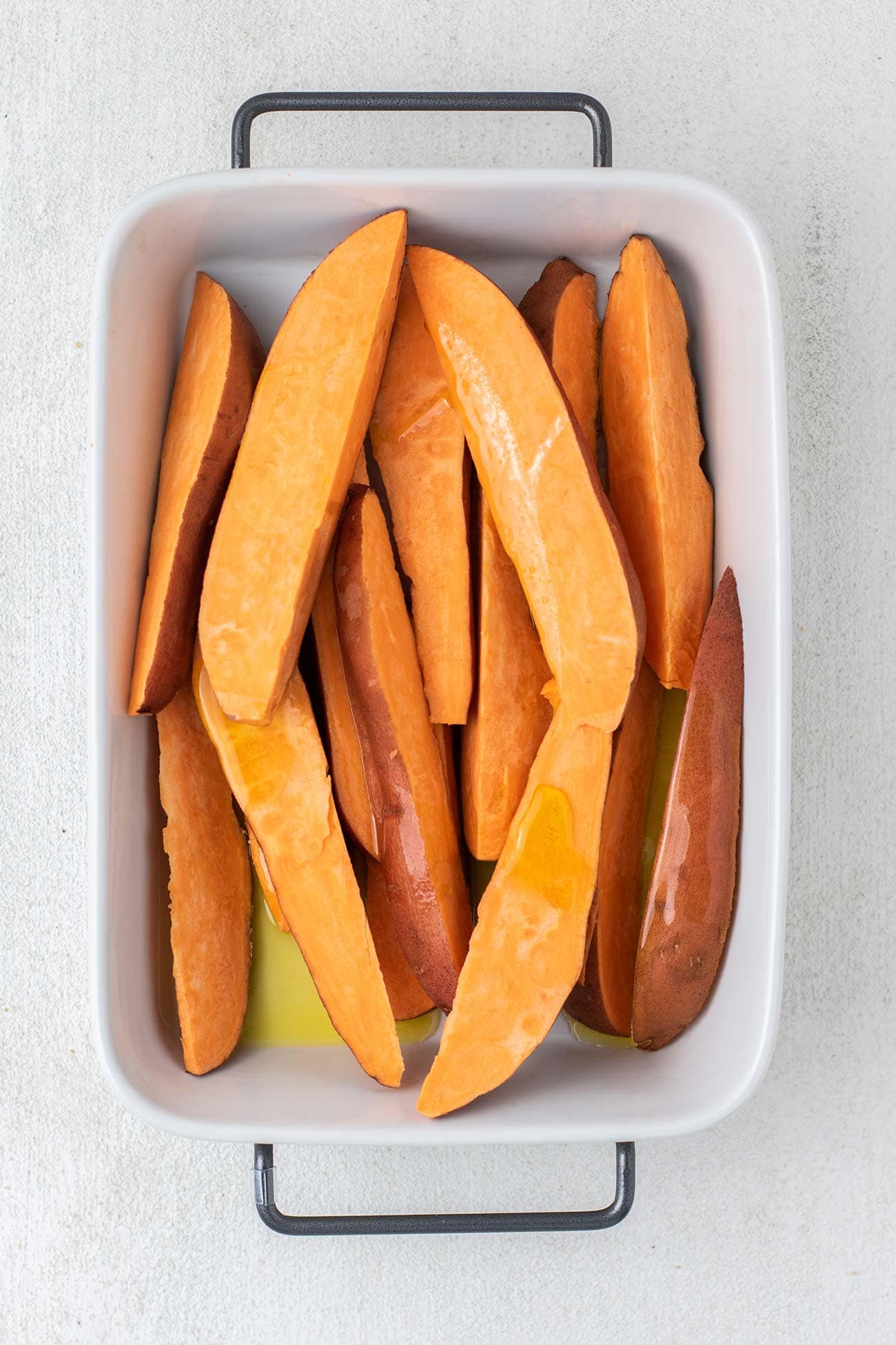 Sweet potatoes cut in wedges being drizzled with olive oil.