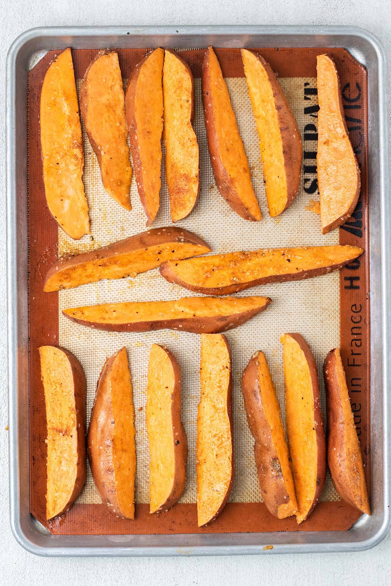 Showing how to add sweet potatoes to a baking tray with space around each one to crisp.