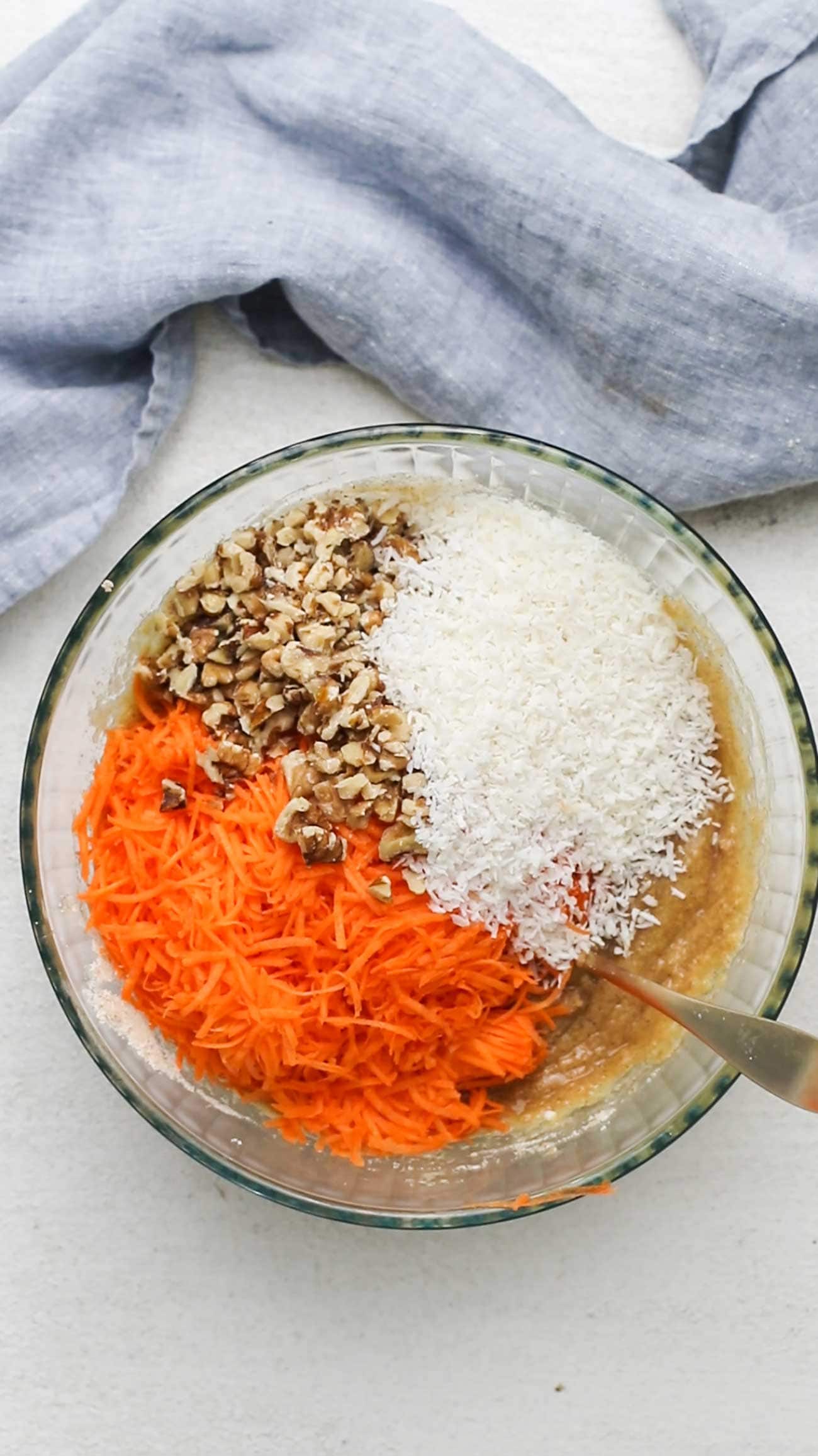 The carrots, walnuts, and coconut being added to the cake mixture.