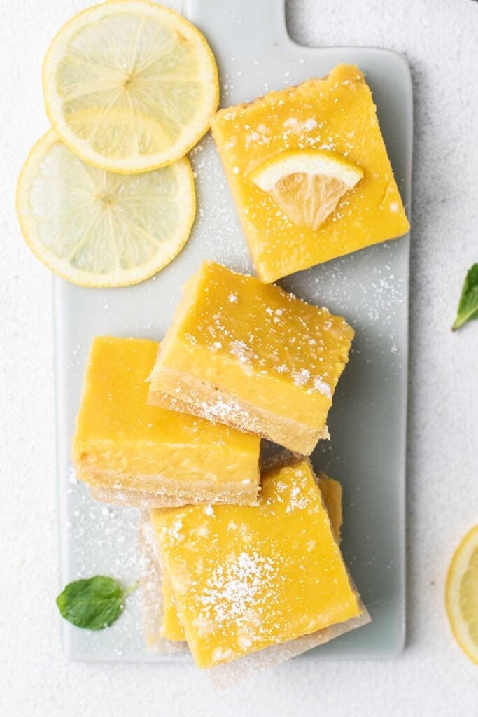 A top down look at lemon squares being served on a cutting board, garnished with powdered sugar.