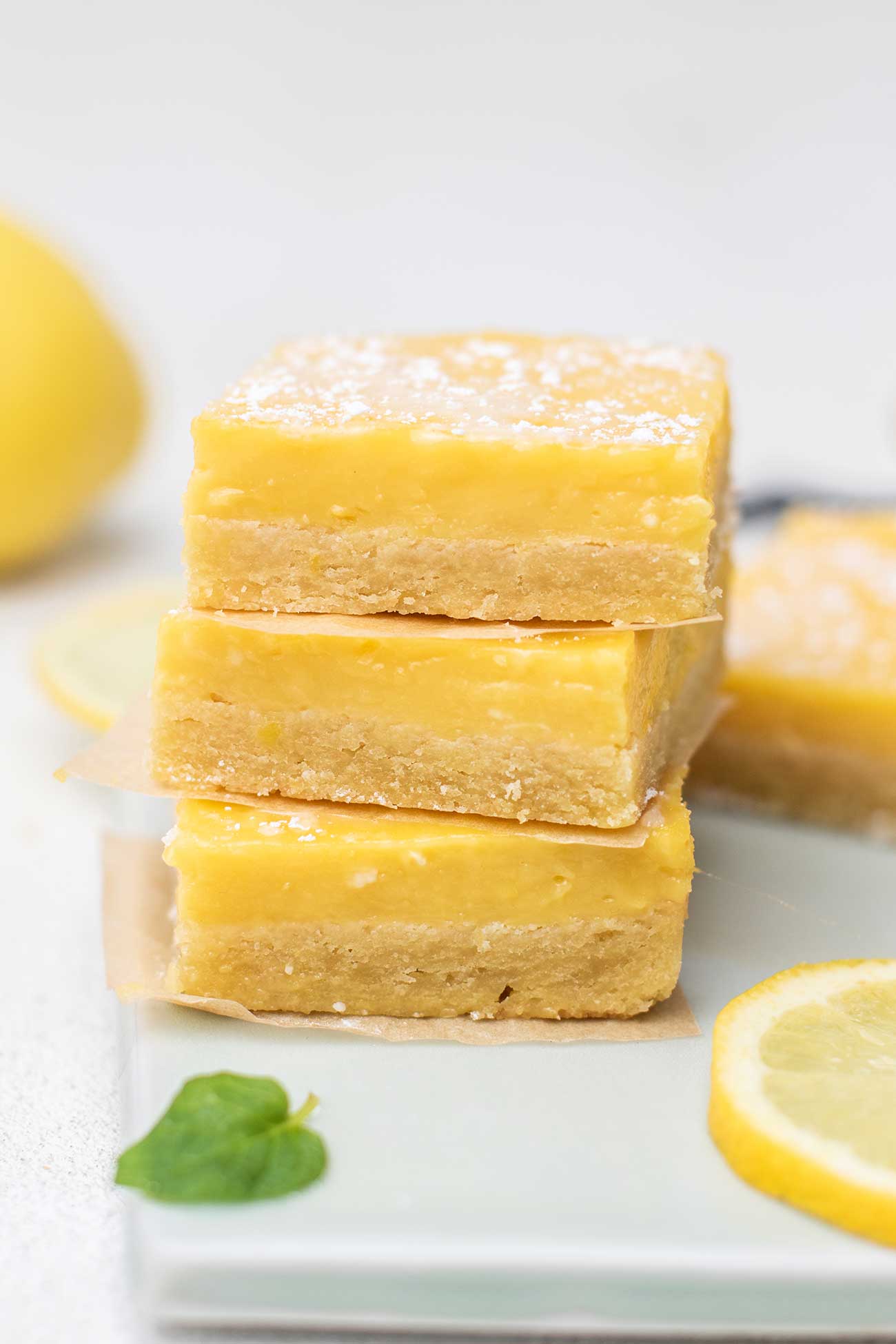 A stack of 3 gluten free lemon bars stacked on a blue cutting board.