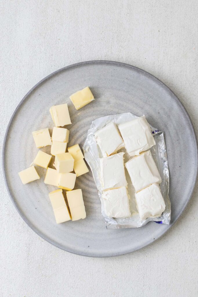 Butter and cream cheese cut into chunks on a plate.