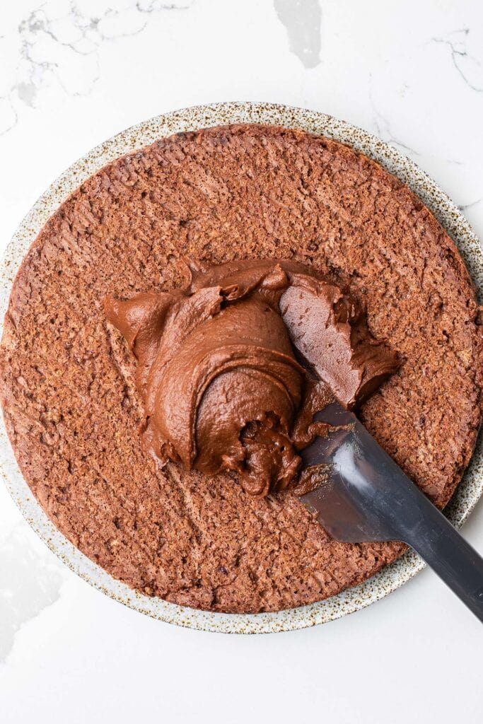 The quinoa cake removed from the pan shown with frosting being added to the top.