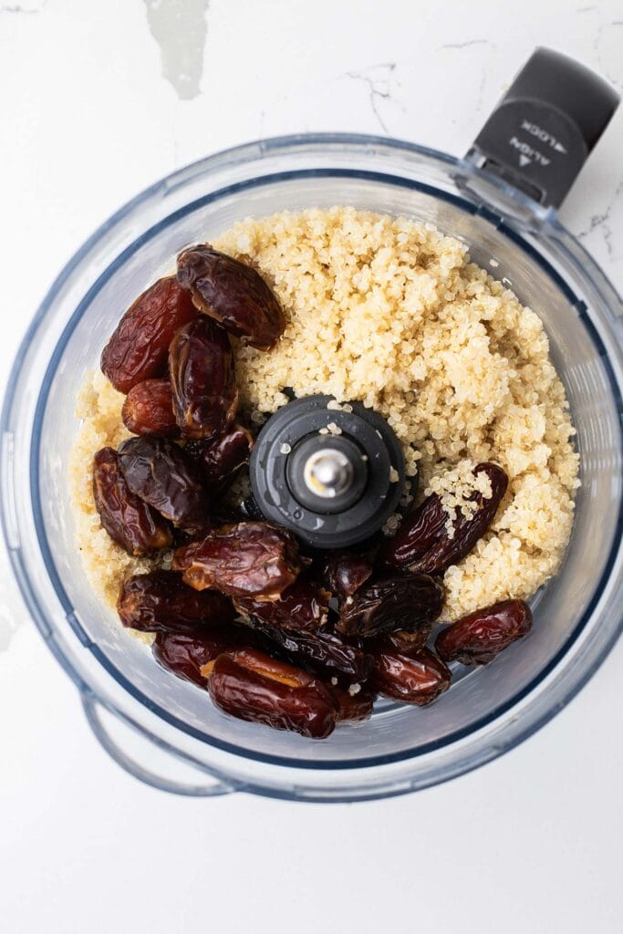 Quinoa and dates added to a food processor bowl.