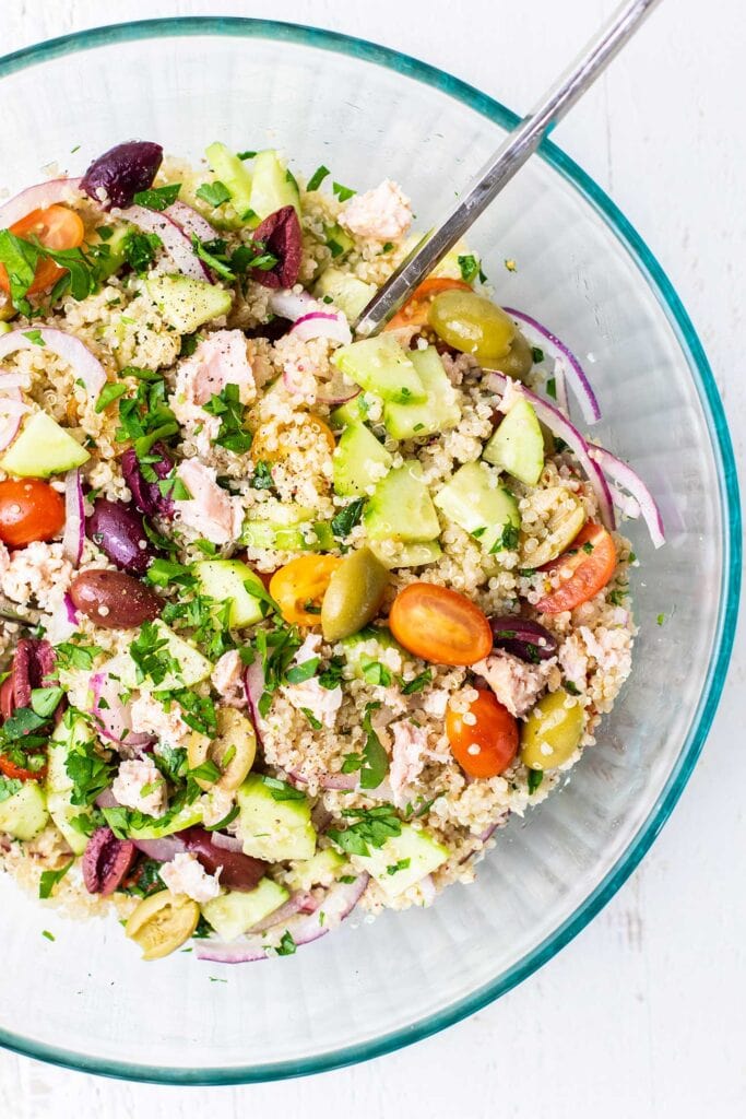 A glass bowl filled with a colorful mediterranean quinoa salad.