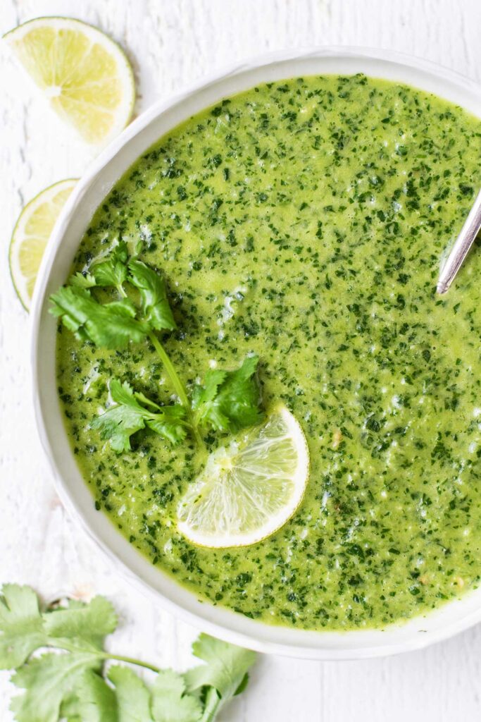 A bowl of mojo verde garnished with cilantro and a lime.