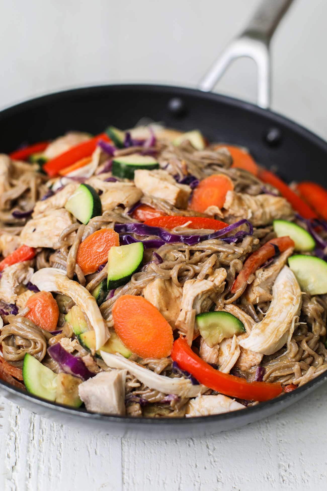 A soba noodle stir fry with colorful veggies mixed in in a large skillet.