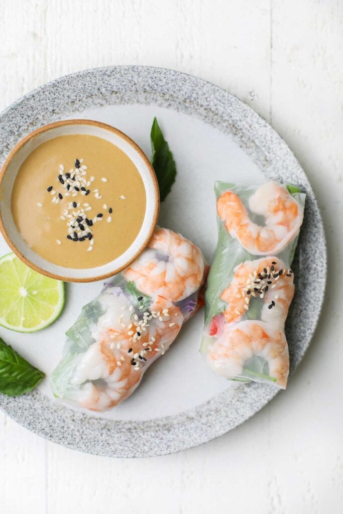 Spring rolls on a plate with a little dish of the peanut sauce.